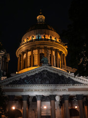 St. Isaac's Cathedral in St. Petersburg. Illuminated church dome at night with statues and inscription. Architectural grandeur.