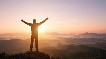 Fototapeta premium Silhouetted man with arms raised in celebration on a rocky outcrop against a vibrant sunrise over misty hills