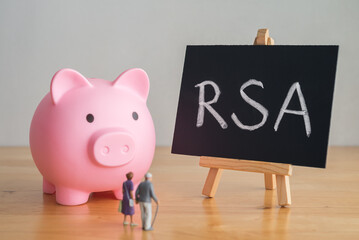 Senior couple looking at RSA (retirement savings account) text writing on blackboard with pink piggy bank on wooden table. Financial planning for elder, money risk management and so on concept.