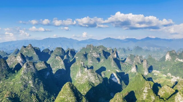 Aerial time-lapse of dramatic karst peaks in Yangshuo, Guilin, China. Lush green mountains under a bright blue sky with scattered clouds.