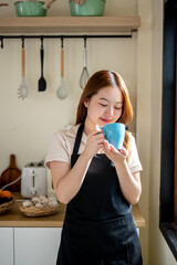 An Asian woman is happily drinking her morning coffee in the kitchen.