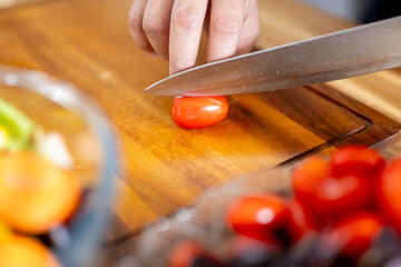 An Asian woman is slicing tomatoes on a kitchen table to make a salad. The imagery relates to healthy eating and dieting.