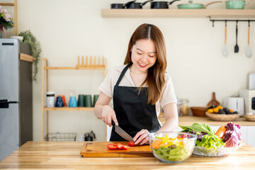 An Asian woman is slicing tomatoes on a kitchen table to make a salad. The imagery relates to healthy eating and dieting.