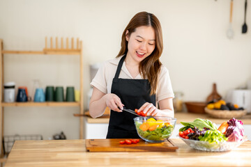 An Asian woman is making a salad in the kitchen. The concept is related to healthy eating and dieting.