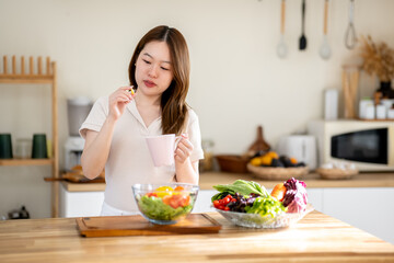 An Asian woman is taking vitamins in the kitchen. The concept of healthy eating and dieting.