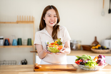 An Asian woman is making a salad in the kitchen. The concept is related to healthy eating and dieting.