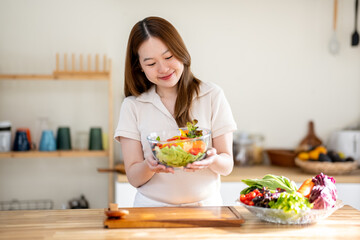 An Asian woman is making a salad in the kitchen. The concept is related to healthy eating and dieting.
