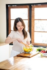 An Asian woman is making a salad in the kitchen. The concept is related to healthy eating and dieting.