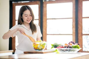 An Asian woman is making a salad in the kitchen. The concept is related to healthy eating and dieting.