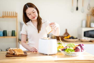 An Asian woman is happily toasting bread for breakfast in the kitchen.