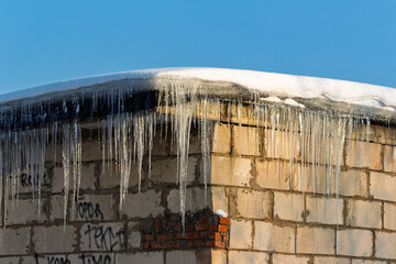 Sharp icicles hang from a snow-capped garage roof against a bright blue winter sky