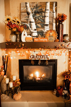 cozy indoor fireplace decorated for Thanksgiving with seasonal garlands, pumpkins, a grateful sign, candles, autumn flowers, and warm orange lighting