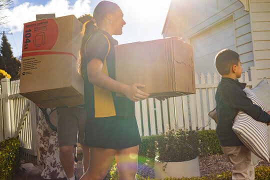 Children with mixed ethnicity carrying cardboard boxes and pillows inside picket fence on moving day