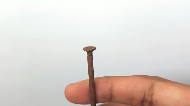 Man holding a rusty metal nail against a white background. Close-up of corroded old iron nail, symbol of tetanus risk, construction decay, and oxidation process