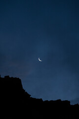 silhouette of mountains with a crescent moon, lots of empty space, blue night sky, dark evening © krista
