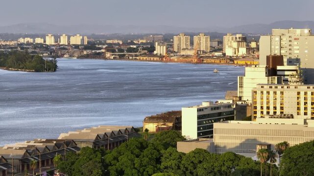 Aerial drone telephoto view showing parallax effect of Porto Alegre city skyline, historic port warehouses and Guaiba Lake during sunset. Shot with 166mm 7x zoom lens in Brazil.