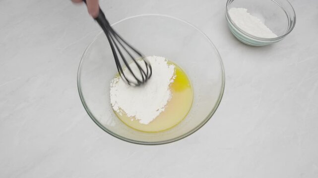 Flour is added to a glass bowl and mixed with a whisk to prepare lemon cake batter.