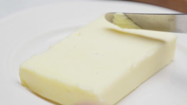 Close-up of a knife scooping soft butter from a butter block during food preparation.