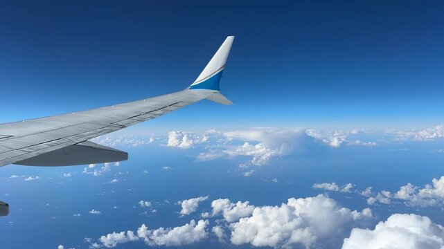Passenger window view of a commercial airplane Boeing 737 Max wing above scattered clouds in a clear blue sky at cruising altitude, calm travel background