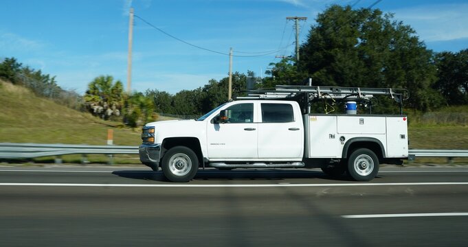 Lakeland, Florida, U.S - Jan 2, 2026 - A white heavy-duty utility truck with a service bed and ladder rack travels quickly along a sunlit highway.