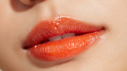 Extreme close-up: Shiny, plump orange-red lips with visible teeth Glossy finish highlights the vibrant color and smooth skin