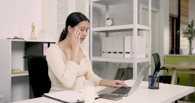 asian pregnant woman touching temple feeling discomfort while working on laptop in home office portraying emotional and physical changes of late pregnancy during routine work from home