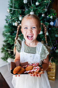 Happy little girl with plate of candy canes and homemade ginger biscuits and tam tams