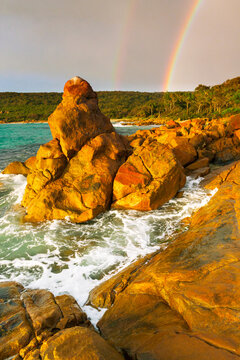 Dramatic storm lighting and a double rainbow over colourful coastal rock formations