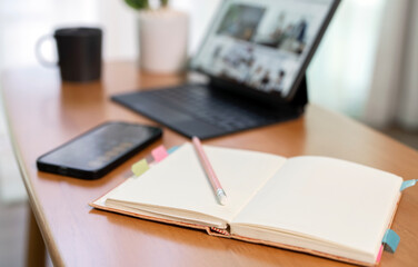 Close-up of an open blank notebook with a pencil on a wooden desk, with a blurred smartphone and tablet in the background, symbolizing education, strategy, and creative goal setting.