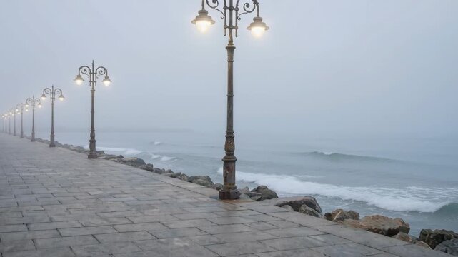 Row of Vintage Lampposts Along a Cobblestone Pathway Beside a Misty Ocean on a Gloomy Overcast Day With Gentle Waves and Rocks