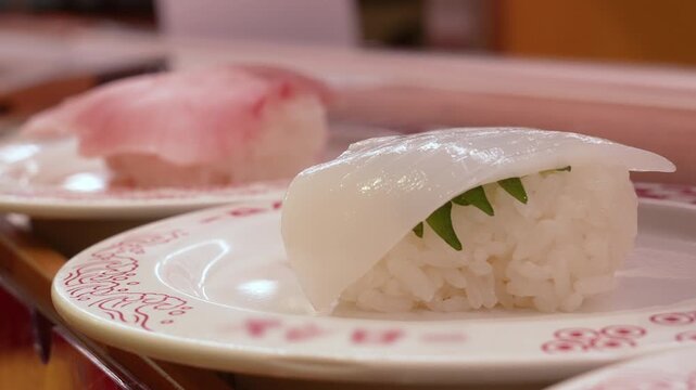 Fresh squid nigiri sushi with shiso leaf on a revolving plate