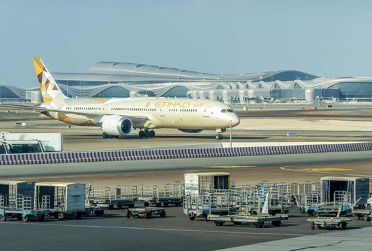 Etihad Boeing 787 Dreamliner taxiing at AUH with terminal and ground service equipment in view.
