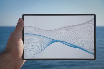 Hand holding tablet with graph over ocean