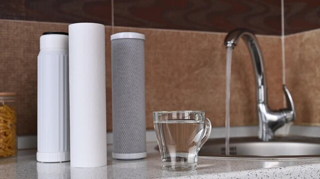 Several cartridges for water filter and glass of water on kitchen table.