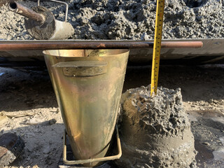 Concrete slump test at construction site. Metal cone lifted, fresh concrete collapses, and slump height is measured to assess mix consistency and workability before placement. © zainul