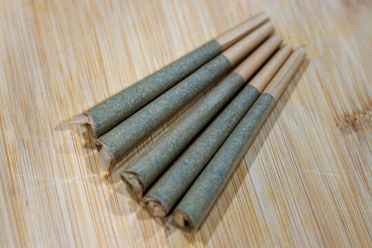 Five pre-rolled cannabis cigarettes on a bamboo cutting board.