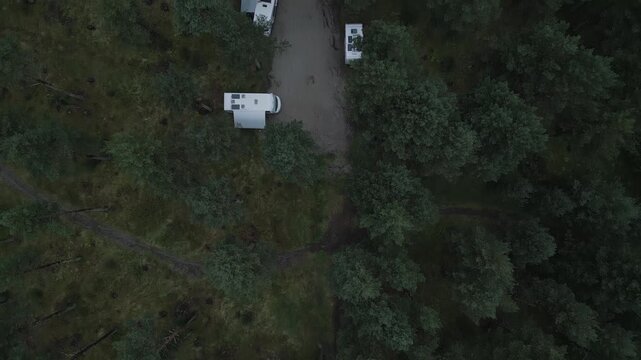 Top-down aerial footage capturing rows of white camper vans and motorhomes parked under the canopy of a lush pine forest at a scenic campsite in the French Pyrenees