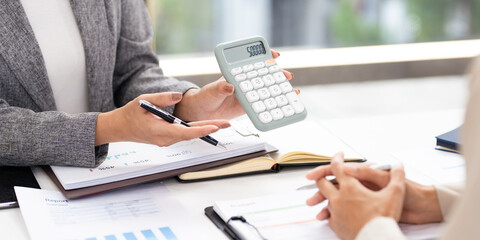 Smiling asian businesswomen financial advisor explaining financial result showing calculator to...