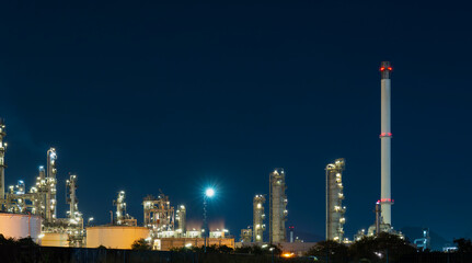 Obraz premium Large industrial petrochemical refinery plant illuminates the night sky with glowing city lights during oil production.