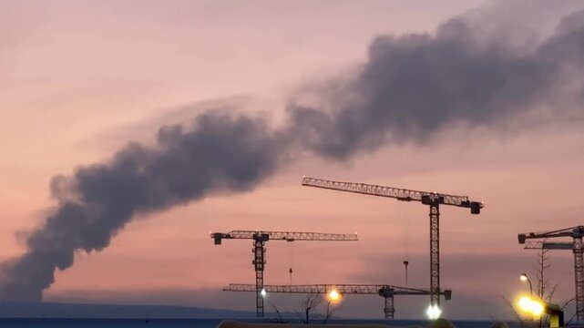 Construction site with towering cranes and multi-story residential buildings under development against a vibrant sunset or sunrise sky. Real estate investment and urban growth concept.
