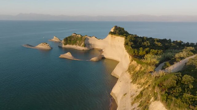 Aerial drone footage of Cape Drastis, Corfu, Greece at golden hour. Flying alongside the dramatic white sandstone cliffs and unique sea stack formations in the Ionian Sea