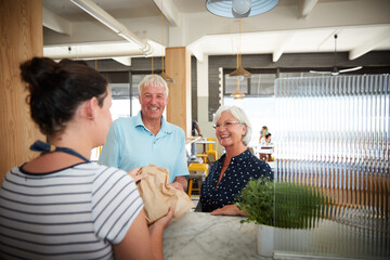 Waitress, serving and senior couple at cafe with food parcel, takeaway order and customer service. Employee, package and elderly people for pickup, friendly interaction and assistance at restaurant © Laflor2000/peopleimages.com