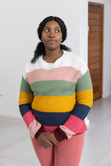 African American woman standing in residential hallway wearing striped sweater and pink leggings