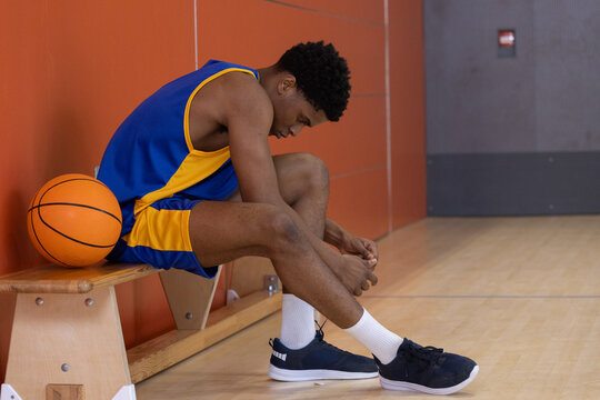 Basketball resting on wooden bench while sneakers are being tied on gym court lines