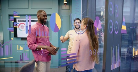 Discussing team in magenta shirt, pink blouse reviewing charts on glass wall with tablet, monitor