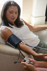 Naklejka premium Hispanic woman patient sitting in chair at home by window while nurse taking blood pressure gauge