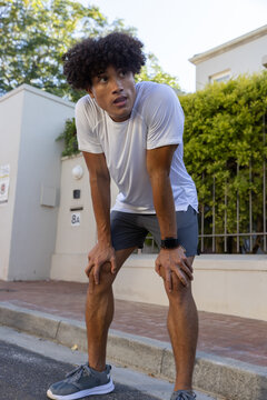 African american man in sportswear leaning forward catching breath on sidewalk