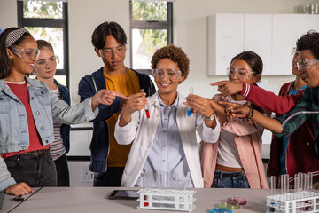 Diverse instructor and students holding test tubes and observing petri dishes, tablet at lab bench