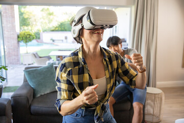 Couple playing virtual reality game in living room on sofa wearing vr headset and gesturing