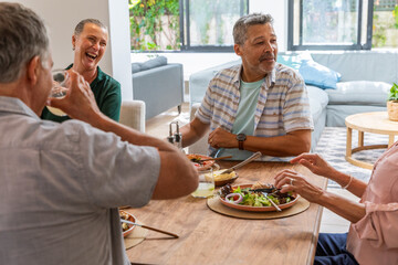 Senior friends raising glasses, eating salad at home dining table with pepper grinder